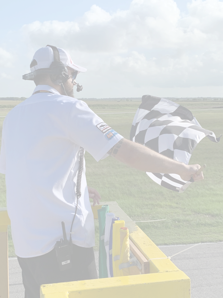 A starter on a yellow flag stand waving the checkered flag over a racetrack.